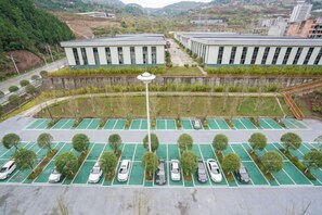 Um estacionamento com várias fileiras de carros estacionados e um edifício com telhado plano ao fundo.