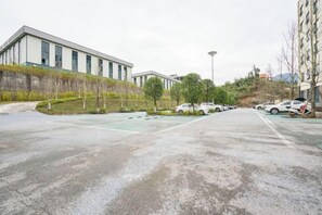 A parking lot with cars, a building with a flat roof, and a grassy area with trees. - Huangyang Hotel (Nanjiang Dejian) (Nanjiang)