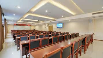 A conference room with rows of chairs and tables, a flat-screen TV, and a red sign on the wall.