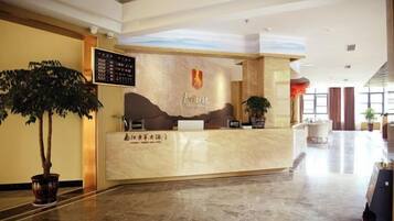 A hotel reception area with a marble counter, a potted plant, and a wall-mounted menu board.