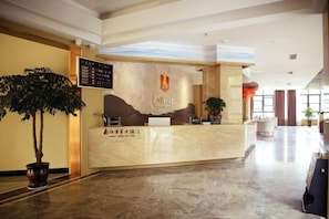 A hotel reception area with a marble counter, a potted plant, and a wall-mounted menu board. - Huangyang Hotel (Nanjiang Dejian) (Nanjiang)