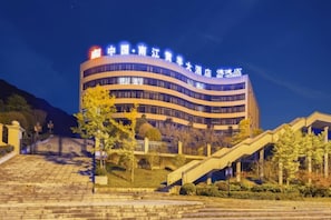 A multi-story hotel with a curved facade, a gated entrance, and a landscaped area with stairs and trees. - Huangyang Hotel (Nanjiang Dejian) (Nanjiang)