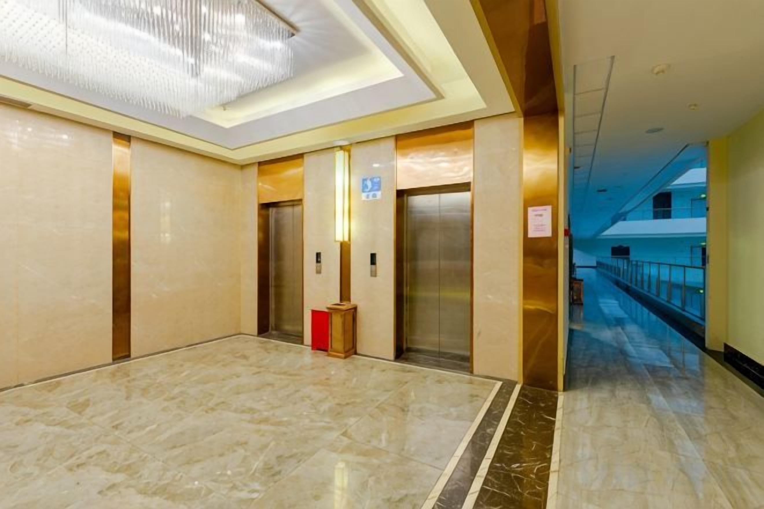 A modern elevator area with marble flooring, a chandelier, and a corridor leading to another section of the building.