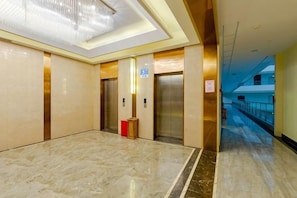 A modern elevator area with marble flooring, a chandelier, and a corridor leading to another section of the building. - Huangyang Hotel (Nanjiang Dejian) (Nanjiang)