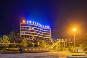 Un edificio de varios pisos con señalización iluminada, un área ajardinada con árboles y una entrada bien iluminada.