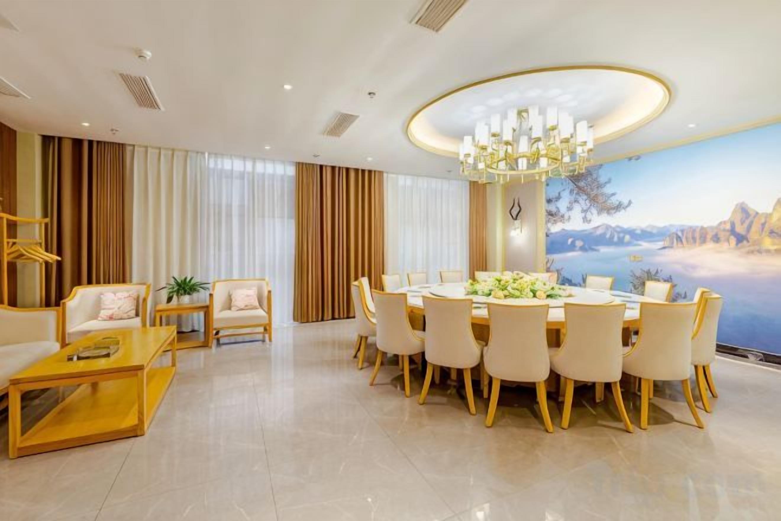 A spacious living room with a dining area, a chandelier, and a large window with curtains.