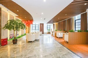Un moderno vestíbulo de hotel con recepción, zona de estar y una planta grande en maceta.