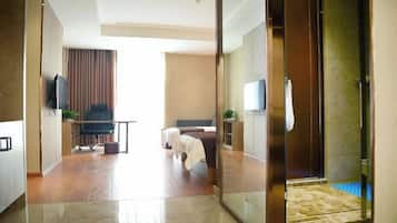 A modern hotel room with a glass partition, a bed, a desk, and a television.