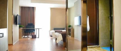 A modern hotel room with a glass partition, a bed, a desk, and a television.