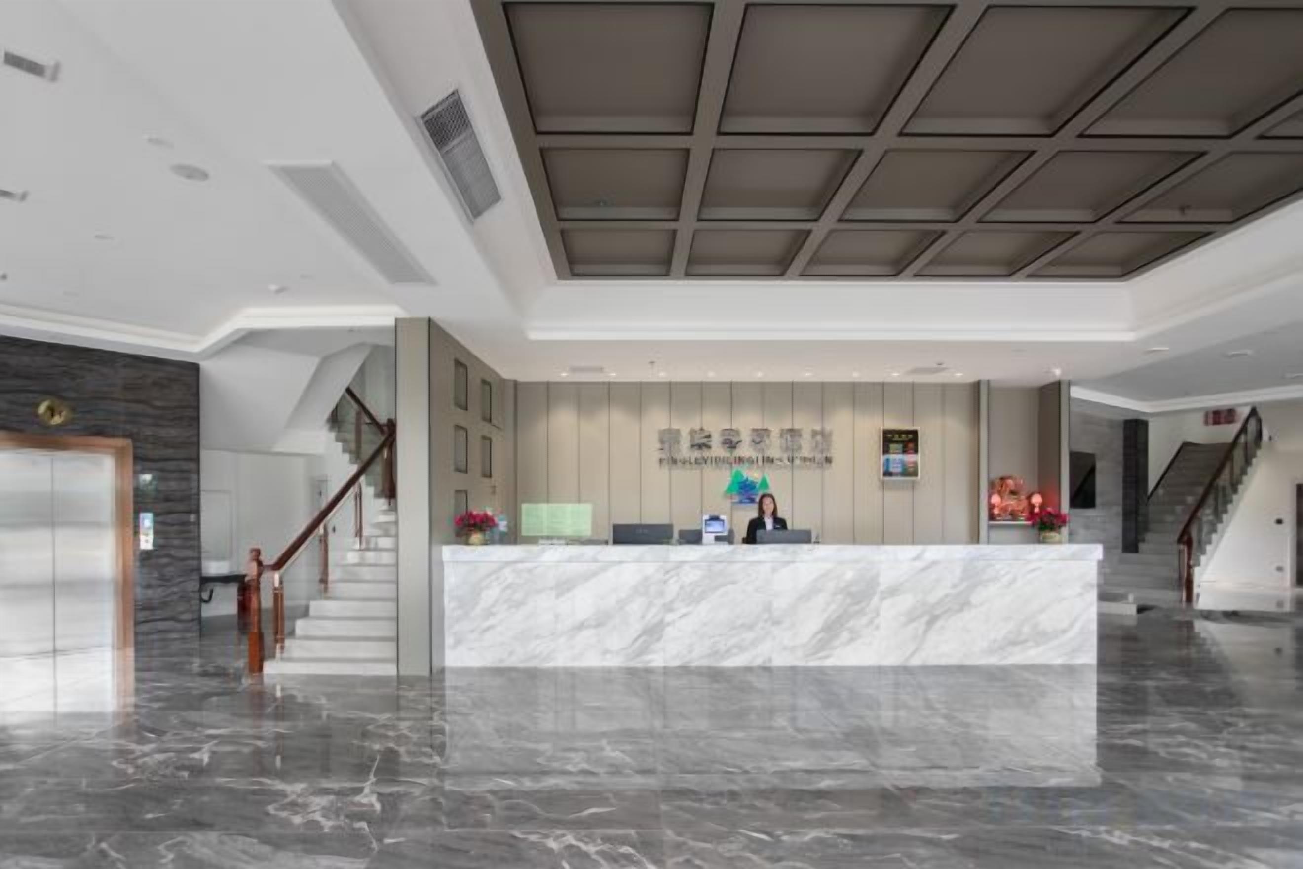 A hotel reception area with a marble counter, a staircase, and a modern ceiling design.