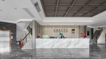 A hotel reception area with a marble counter, a staircase, and a modern ceiling design.
