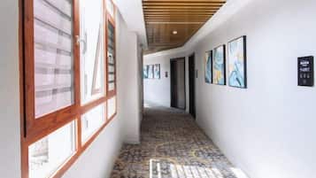 A hallway with patterned flooring, wooden ceiling beams, and framed artwork on the walls.