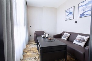 Habitación de hotel con sofá, una mesita con hervidor y alfombra estampada.