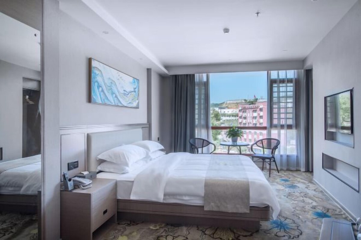 A hotel room with a bed, bedside table, and a view of the city.