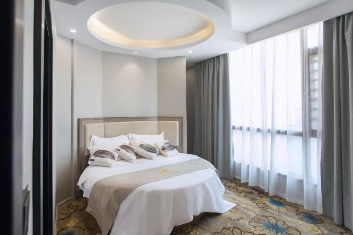 A hotel room with a bed, a ceiling light, and a window with curtains.