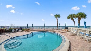 A pool area with lounge chairs and palm trees, surrounded by a fence.