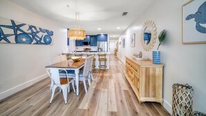 A spacious kitchen with modern appliances, a dining area with a wooden table and white chairs, and a hallway with a decorative mirror and wall art.