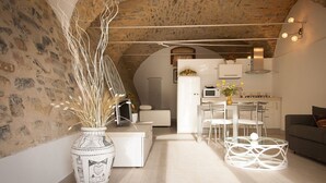 A modern kitchen with white appliances, a dining area with a glass table, and a living space with a sofa and decorative vase. - Housing with private garden terrace and residential swimming pool (Liguria)