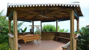 A covered outdoor patio with a wooden structure, a table with a plaid tablecloth, and benches. - Sea view house (bois de nèfles st paul)
