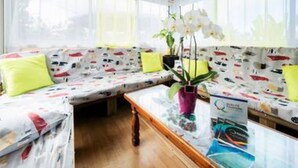 A cozy room with a wooden ceiling, a sofa with patterned cushions, a small table with a plant, and a window with sheer curtains. - Sea view house (bois de nèfles st paul)