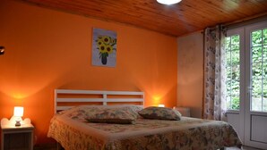 A bedroom with a wooden ceiling, a bed with floral bedding, a nightstand with a lamp, and a window with curtains. - Sea view house (bois de nèfles st paul)