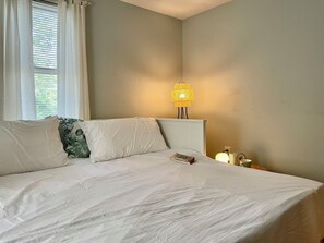 A bed with white bedding, a bedside table with a lamp, and a window with curtains.