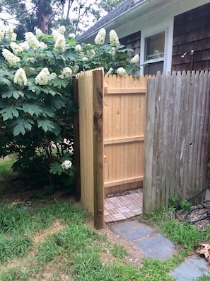 A wooden gate leading to a brick pathway, surrounded by lush greenery and a wooden fence.