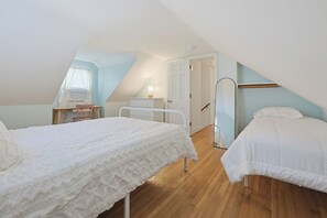A bedroom with two beds, a desk, a chair, a wardrobe, and a door leading to another room.
