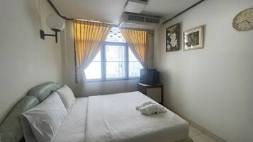 A hotel room with a bed, a television on a small table, a window with curtains, and a wall clock.