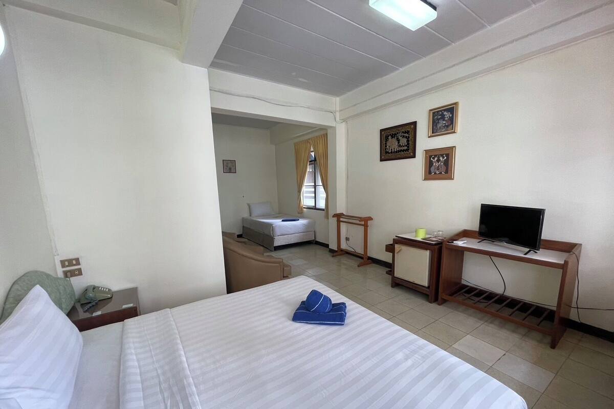 A hotel room with a bed, a desk with a television, a chair, and a small table.