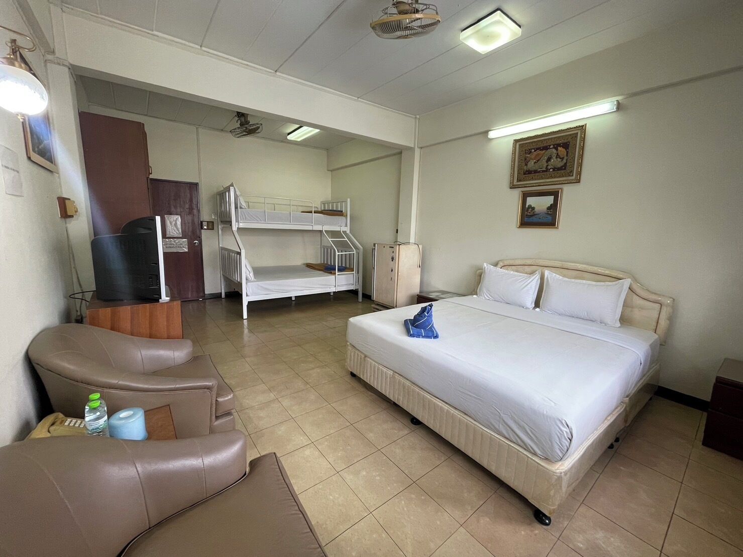 Une chambre d’hôtel avec un lit superposé, un lit simple, un bureau avec un ordinateur, une chaise et un canapé.