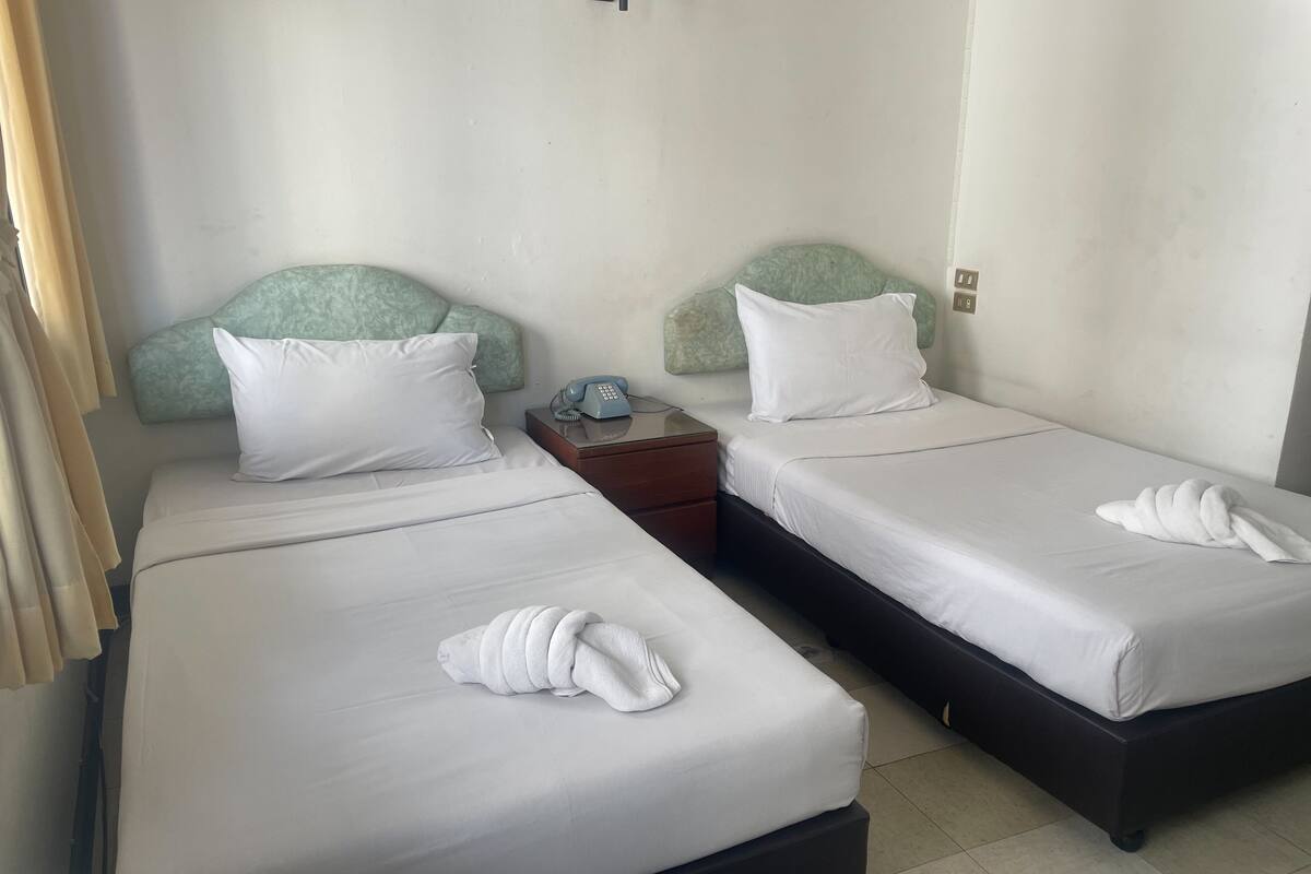 A hotel room with two single beds, each with a pillow and a neatly folded towel.