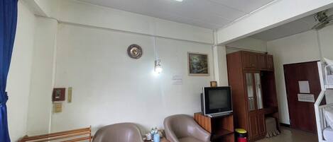 A living room with two leather armchairs, a television on a wooden stand, a fan, and a small table with bottles.