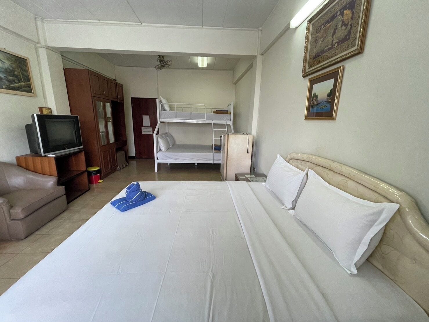A hotel room with a large bed, a TV, a bunk bed, and a desk.