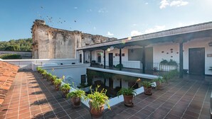 A courtyard with terracotta tiles, potted plants, and a building with a balcony. - Casita Esquinera (Antigua Guatemala)