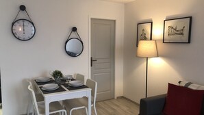 Un coin repas avec une table blanche dressée pour quatre personnes, un miroir, une horloge et une lampe.
