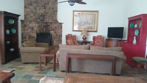 Una sala de estar acogedora con chimenea de piedra, dos sillones, un sofá, una mesa de centro de madera y un armario rojo con objetos decorativos.