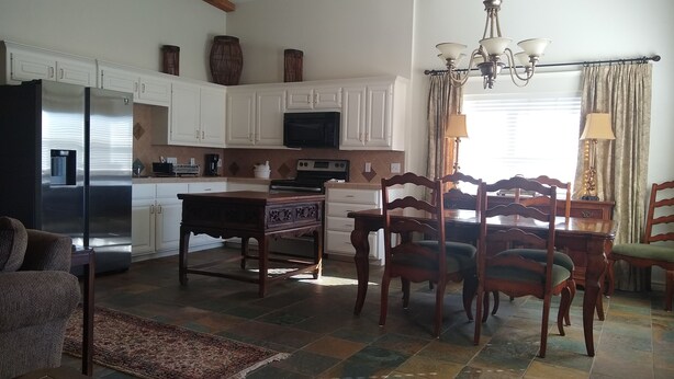 Una cocina amplia con armarios blancos, un comedor con sillas de madera y una mesa, y una araña.