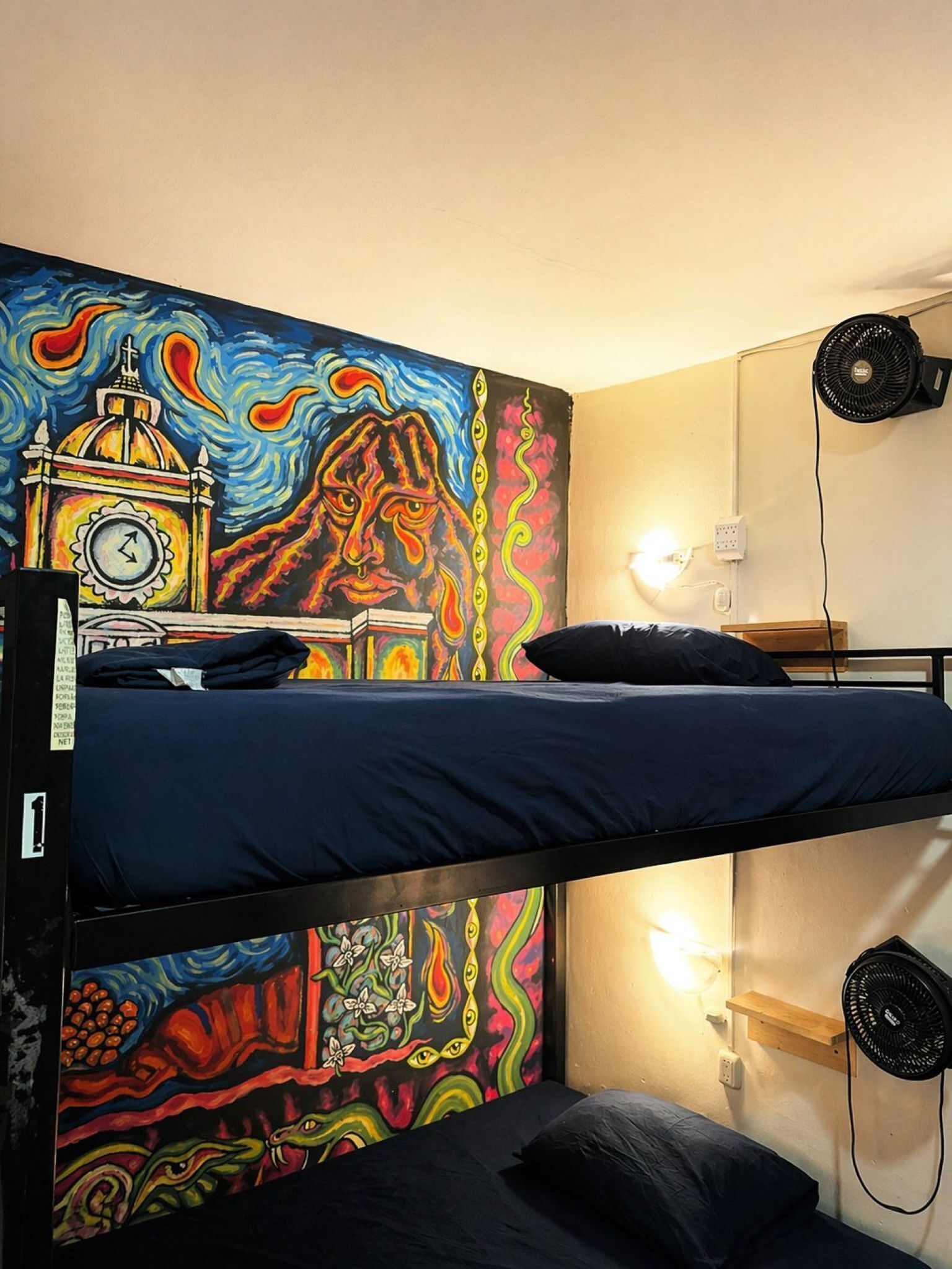 A bunk bed room with a colorful mural, a desk with books, and two wall fans.