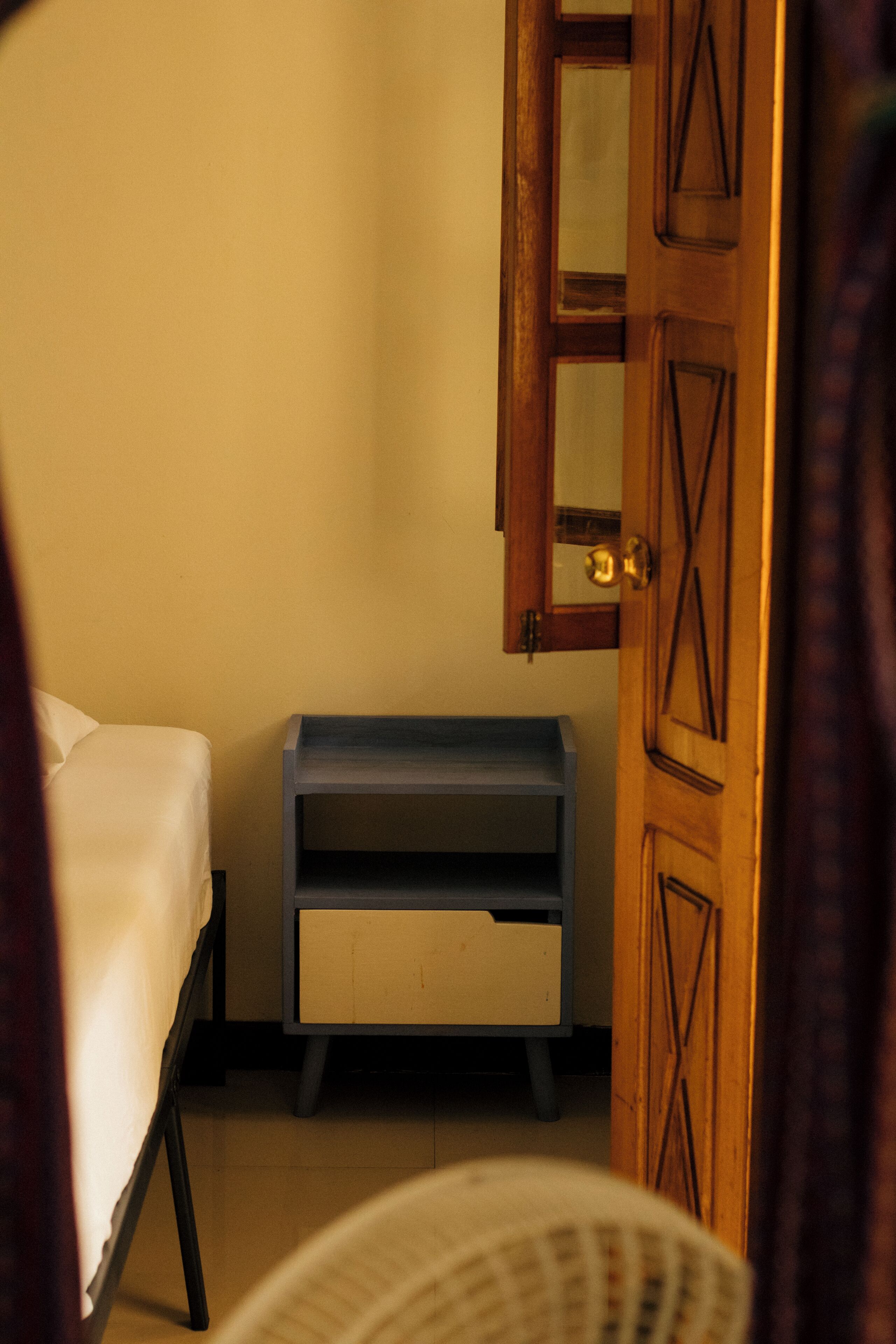 Una stanza con un letto, un comodino in legno, uno specchio e una porta.