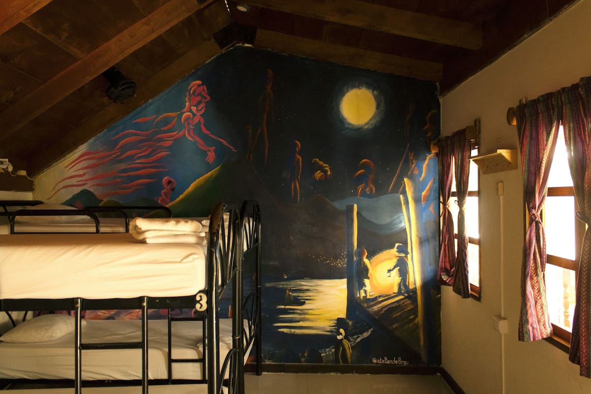 A room with bunk beds, a mural on the wall, and a window with curtains.