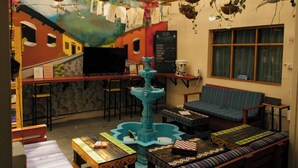 Een knusse bar met een muurschildering, zitplaatsen, een fontein en een prikbord met evenementenaankondigingen.