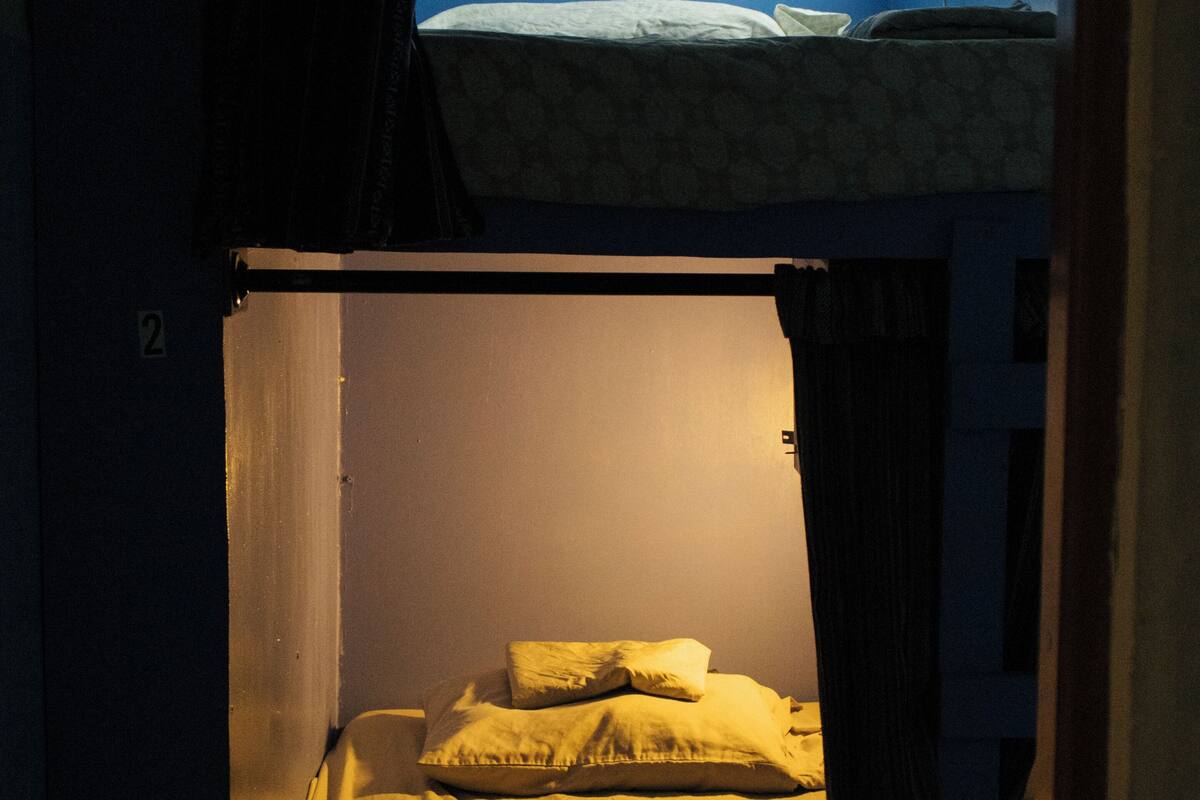 A bunk bed with a mattress and pillows, a curtain, and a wall-mounted light fixture.