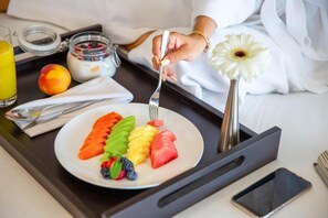 A breakfast tray with a plate of fruit, a glass of orange juice, a jar of yogurt, and a small white flower.