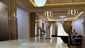 A modern kitchen with a marble countertop, pendant lighting, and a dining area with a table and chairs. - Nigus House Oniru (Lagos)