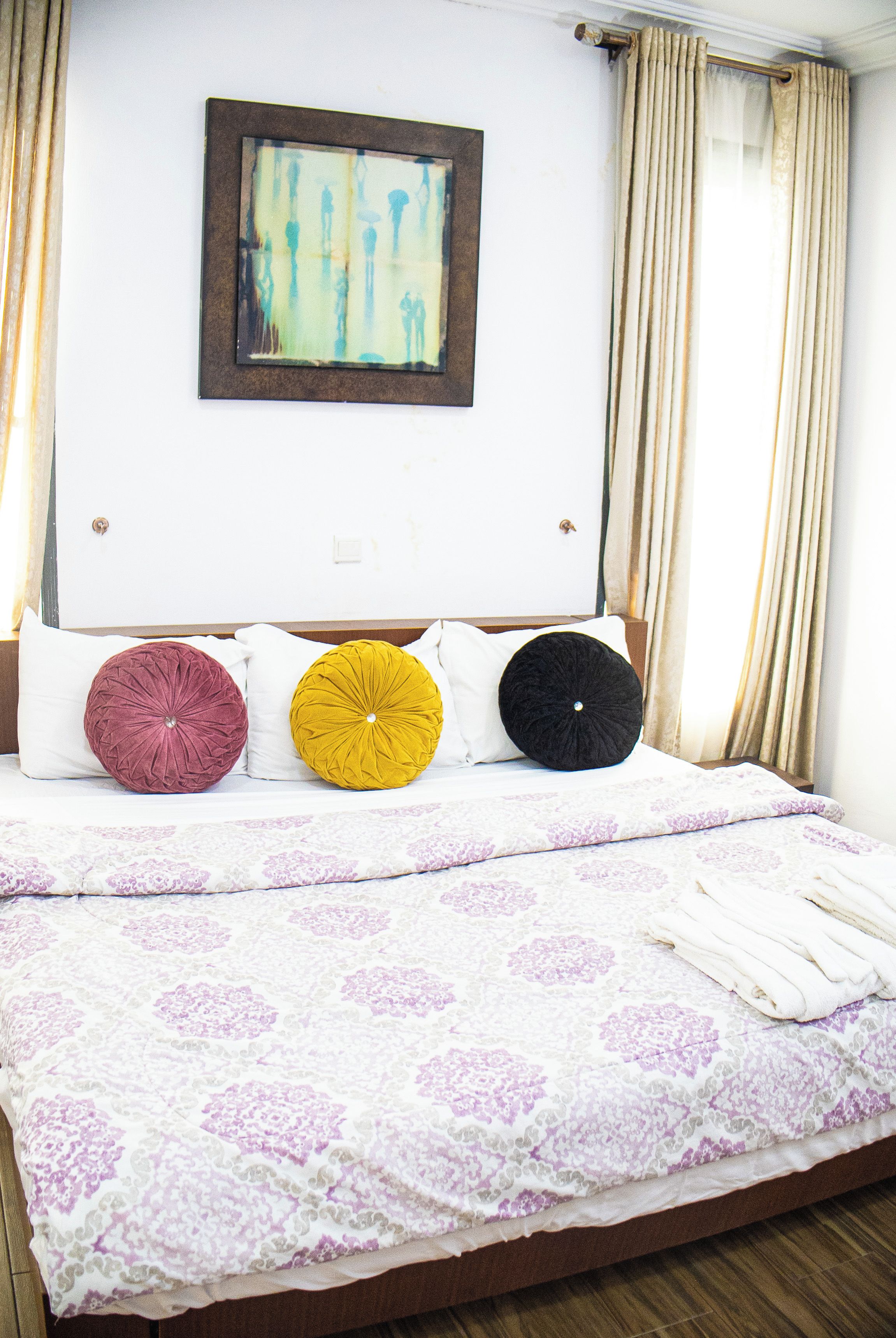 A bed with a patterned bedspread, three pillows, and a framed artwork above.