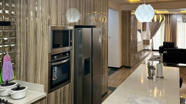 A modern kitchen with built-in appliances, a central island, and a contemporary pendant light. - Nigus House Oniru (Lagos)