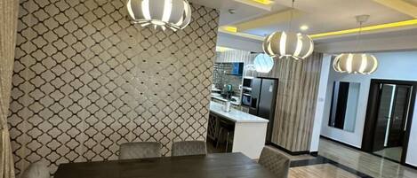 A modern dining area with a rectangular table and six chairs, a patterned wall, and pendant lighting.