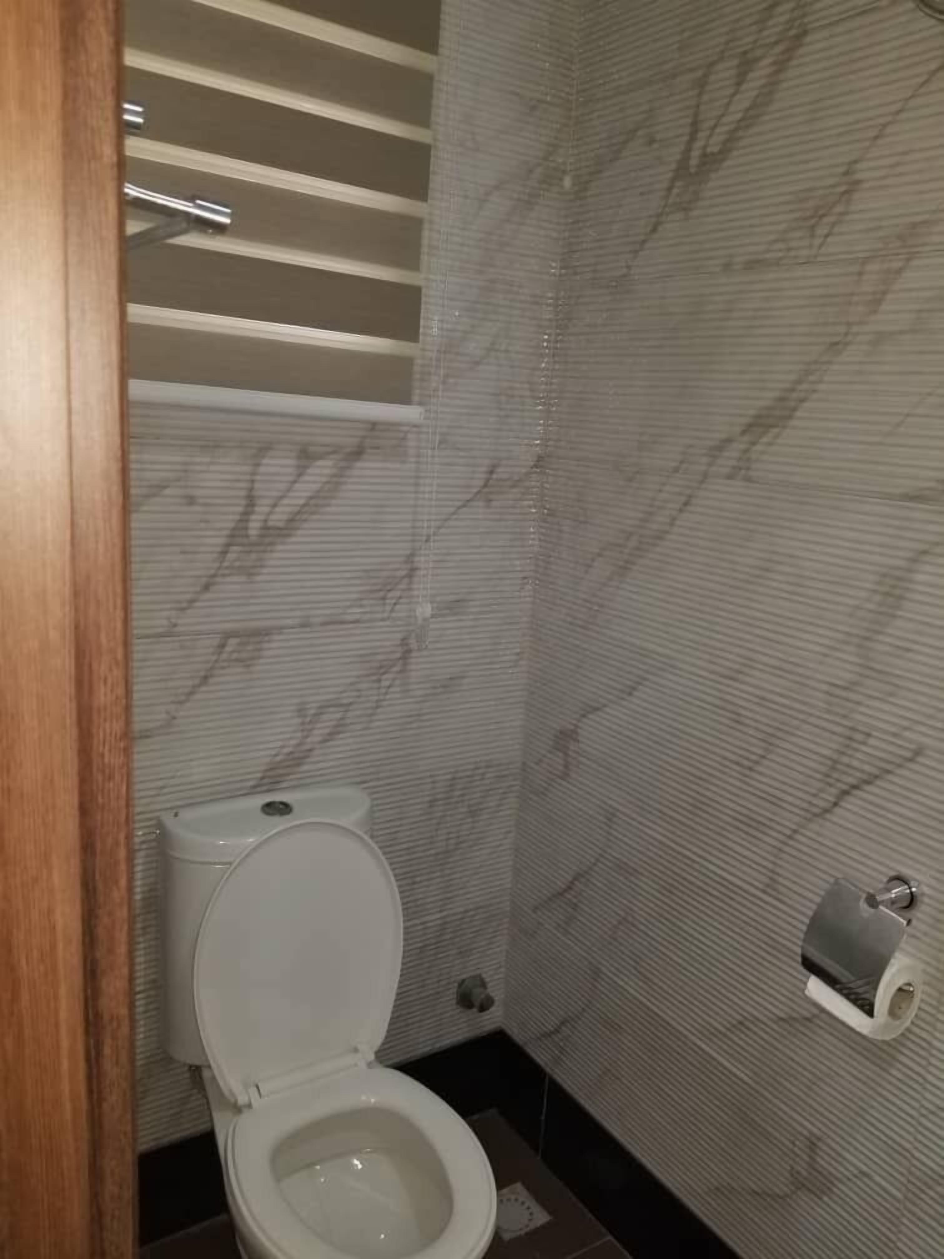 Un bagno con il water, pareti effetto marmo e un portasciugamani.