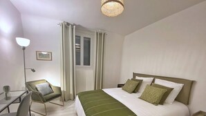 Habitación de hotel con una cama grande, un escritorio con silla, una lámpara y un ventanal con cortinas.